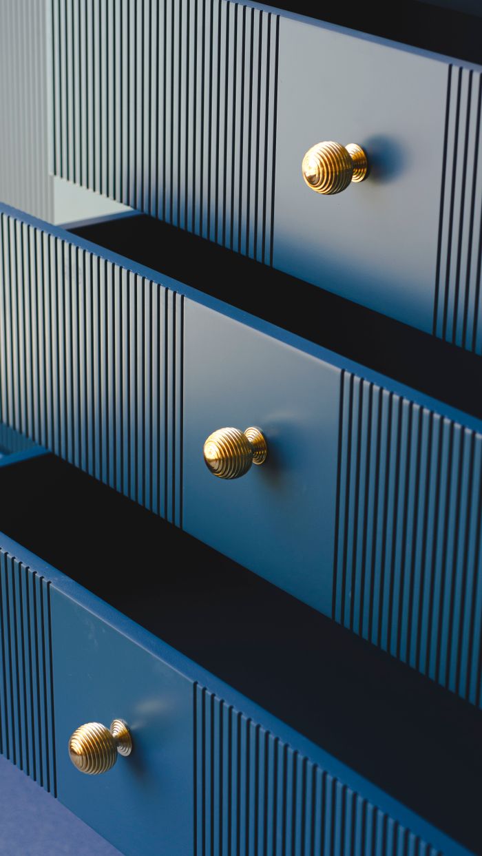 Close-up of a stylish blue dresser with gold knobs, showcasing elegant furniture design.